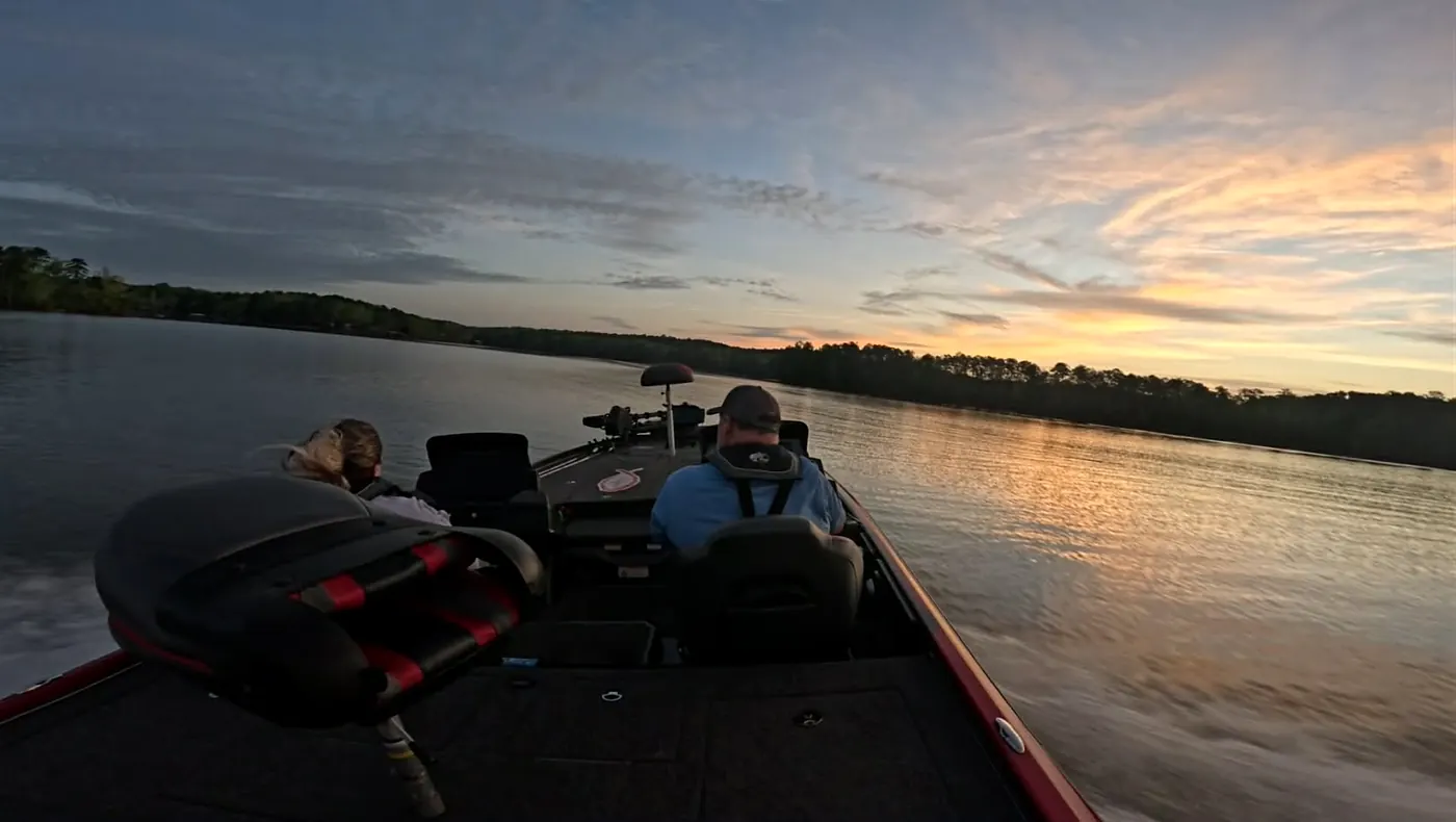 A red bass boat running across a calm lake at sunrise, two anglers aboard